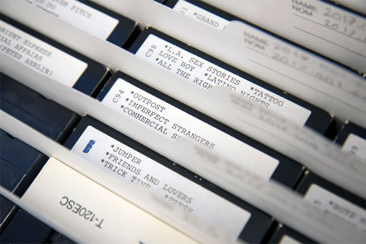Closeup photo of VHS tapes in archival folders. Middle one labeled C94 *OUTPOST *IMPERFECT STRANGERS