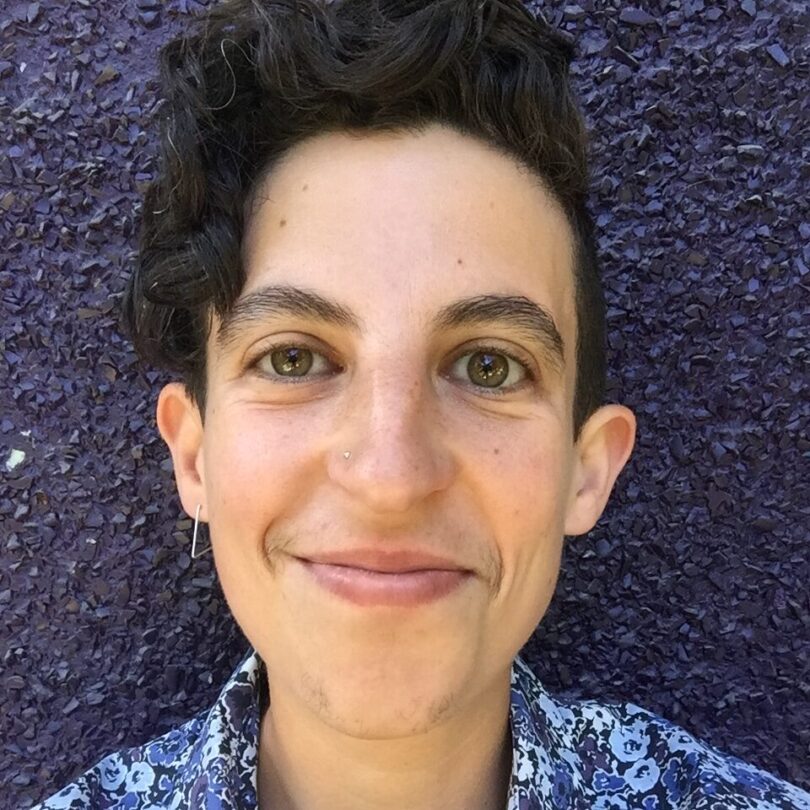 Against a black stucco wall background, LJ smiles broadly at the camera while wearing a blue floral collared shirt.