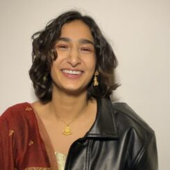 Laila laughs while looking at the camera, wearing gold jewelry and half a leather jacket.