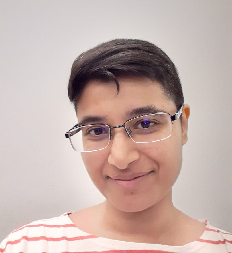 A headshot of Naveen Minai, wearing glasses and a striped shirt and smiling at the camera.