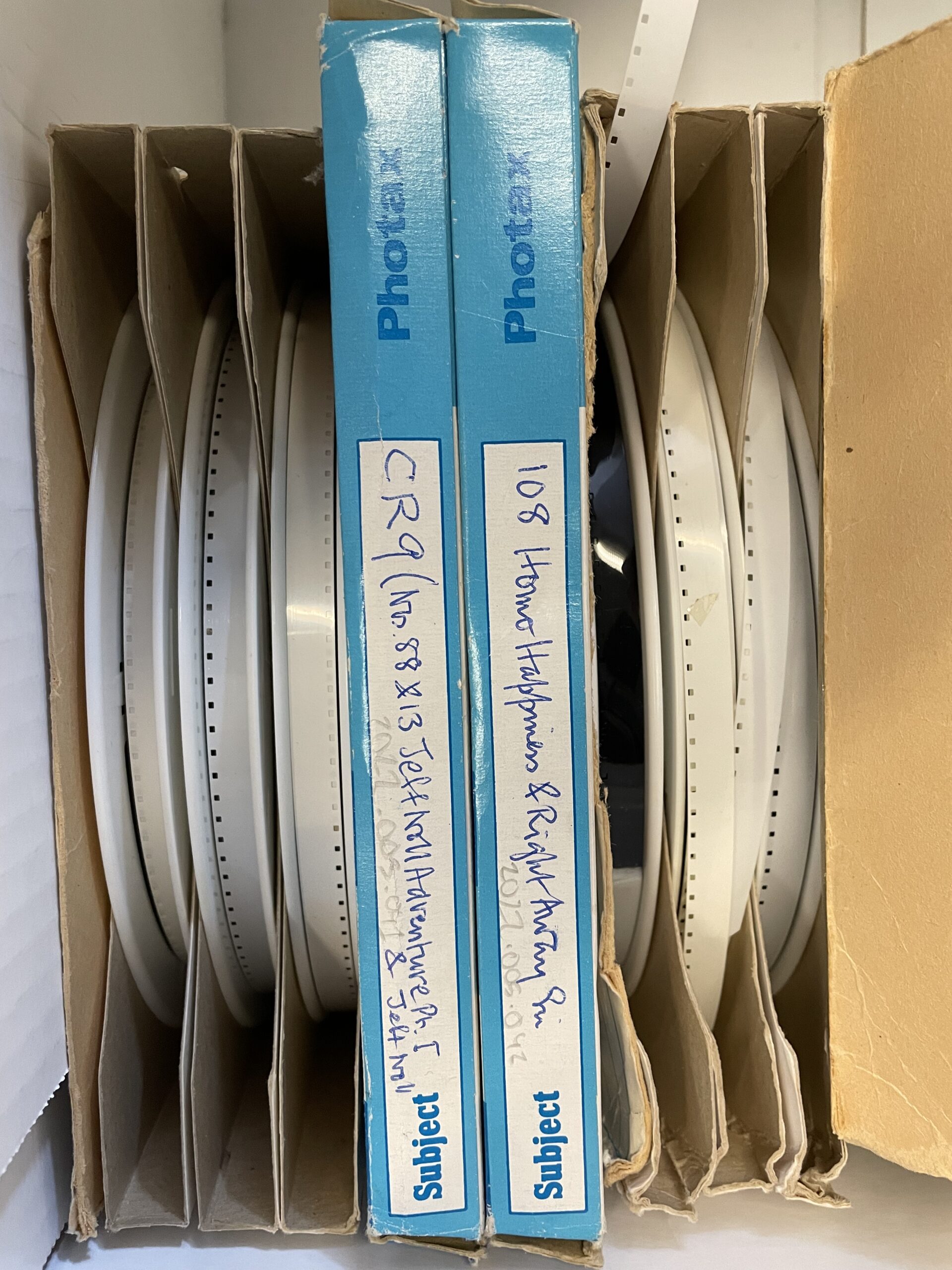 A collection of white film reels stored in blue cardboard boxes