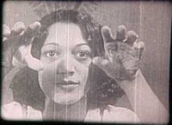 Black and white film still of a woman holding her hands out to the camera as if hypnotizing the viewer.