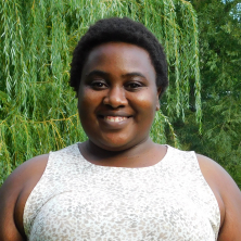 Chido smiles at the camera in a park, wearing a white dress with light patterned print.